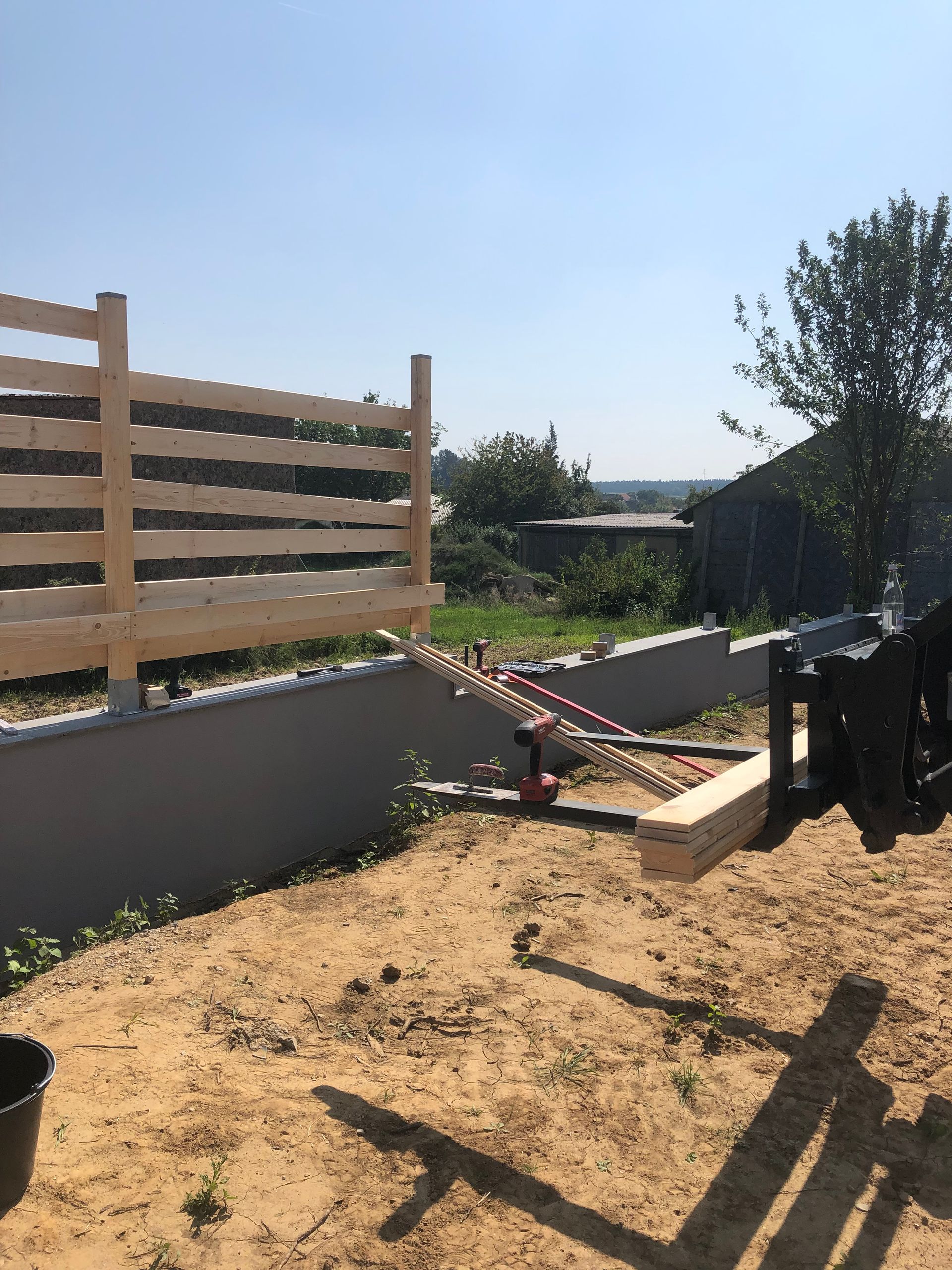 Holzzaunbau an einem sonnigen Tag; Werkzeuge und Materialien liegen auf sandigem Untergrund.