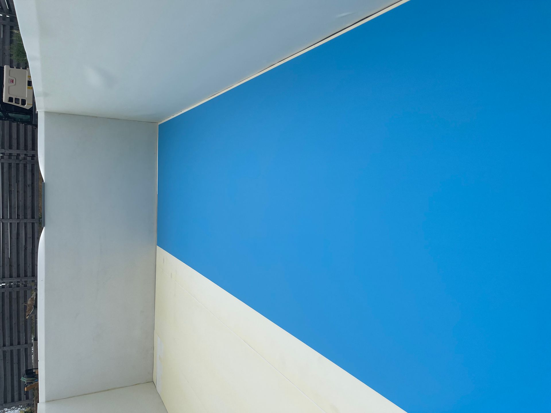 Blau-weiße Wand mit diagonaler Farbaufteilung im Außenbereich.