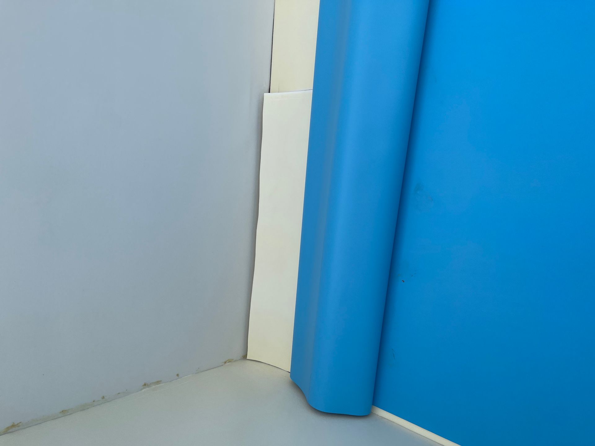 Blaue und graue Wände treffen an einer Ecke aufeinander. Dazwischen steht eine weiße Säule, auf der rechten Seite ein blauer, gepolsterter Wächter.