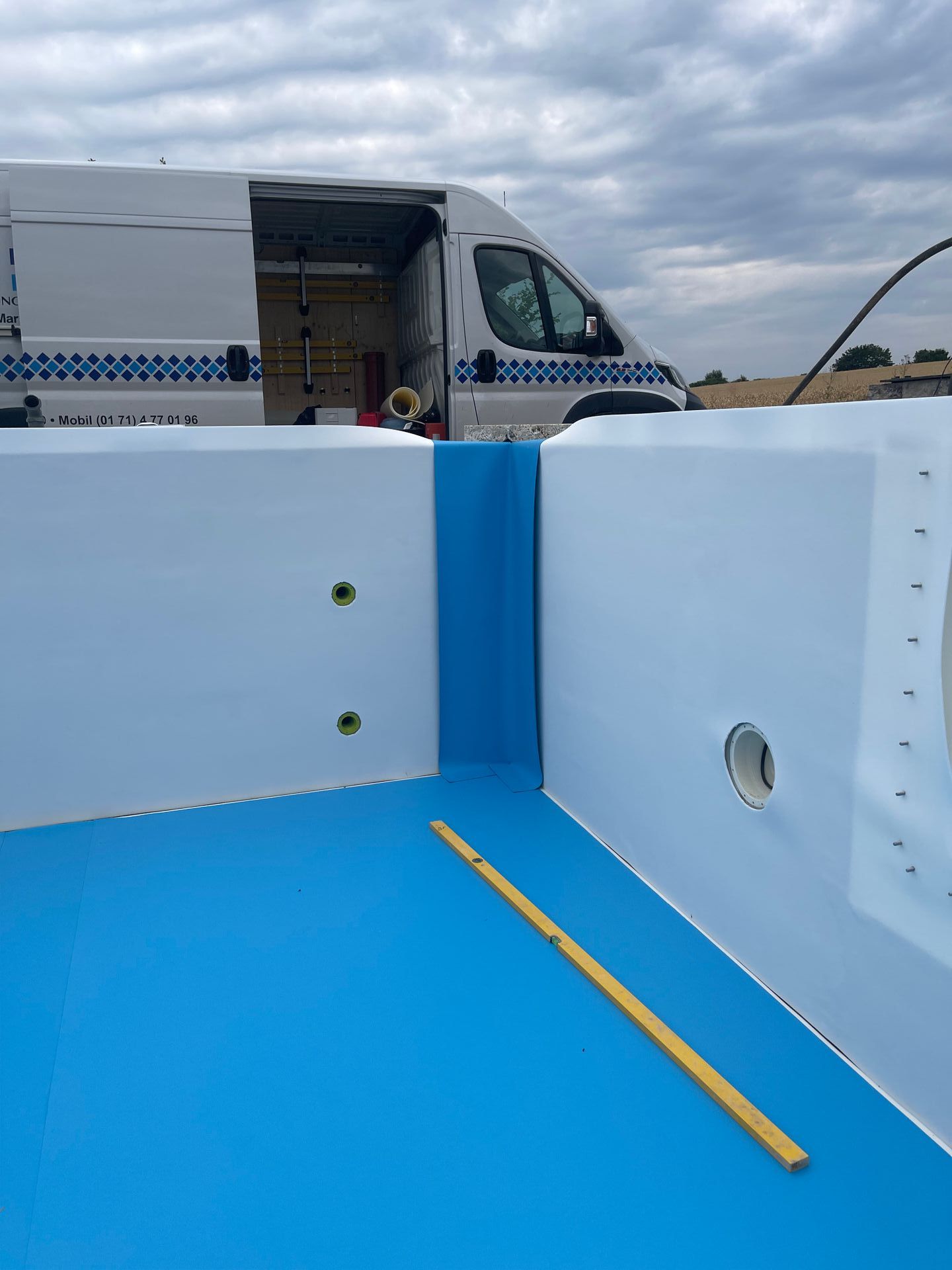 Blaue Poolfolie wird in eine weiße Poolstruktur eingebaut. Lieferwagen im Hintergrund.