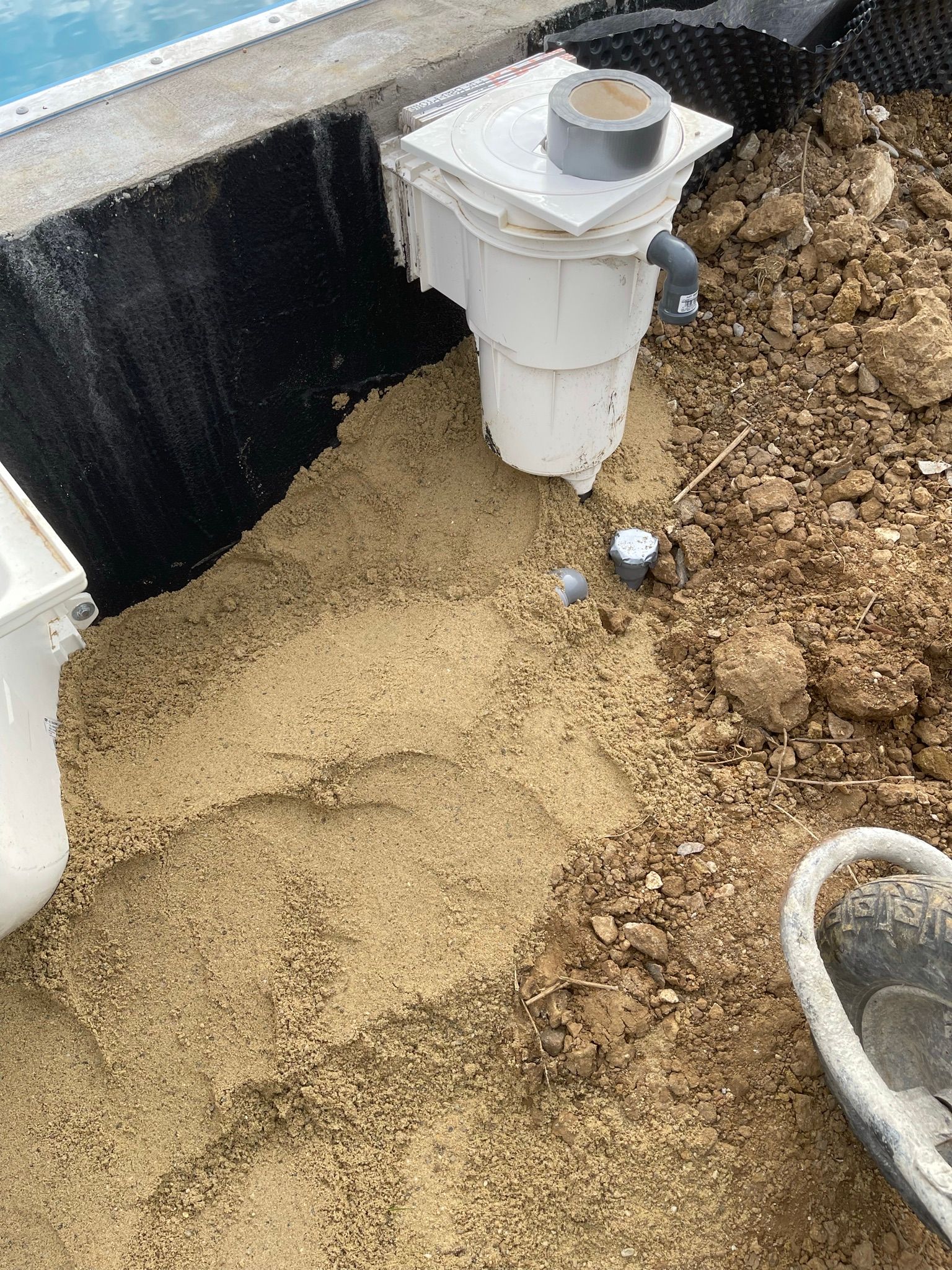 Installation des Pool-Skimmers im Gange, umgeben von Sand und Erde.