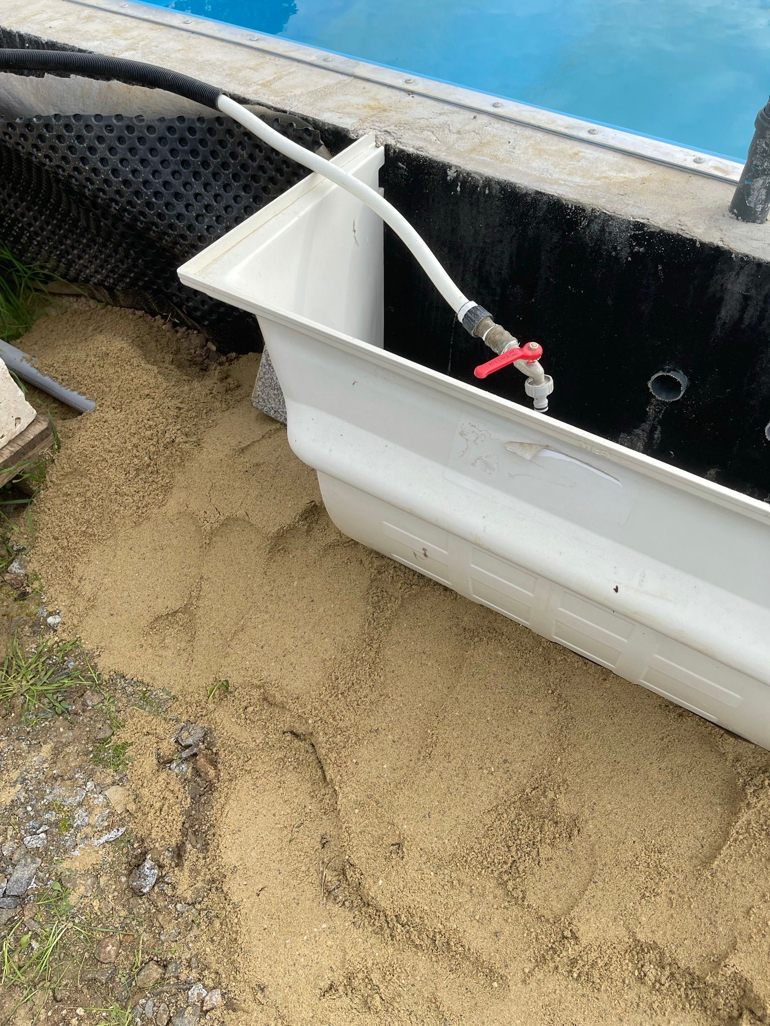 Weiße Poolrinne neben dem mit blauem Wasser gefüllten Pool, umgeben von beigem Sand.