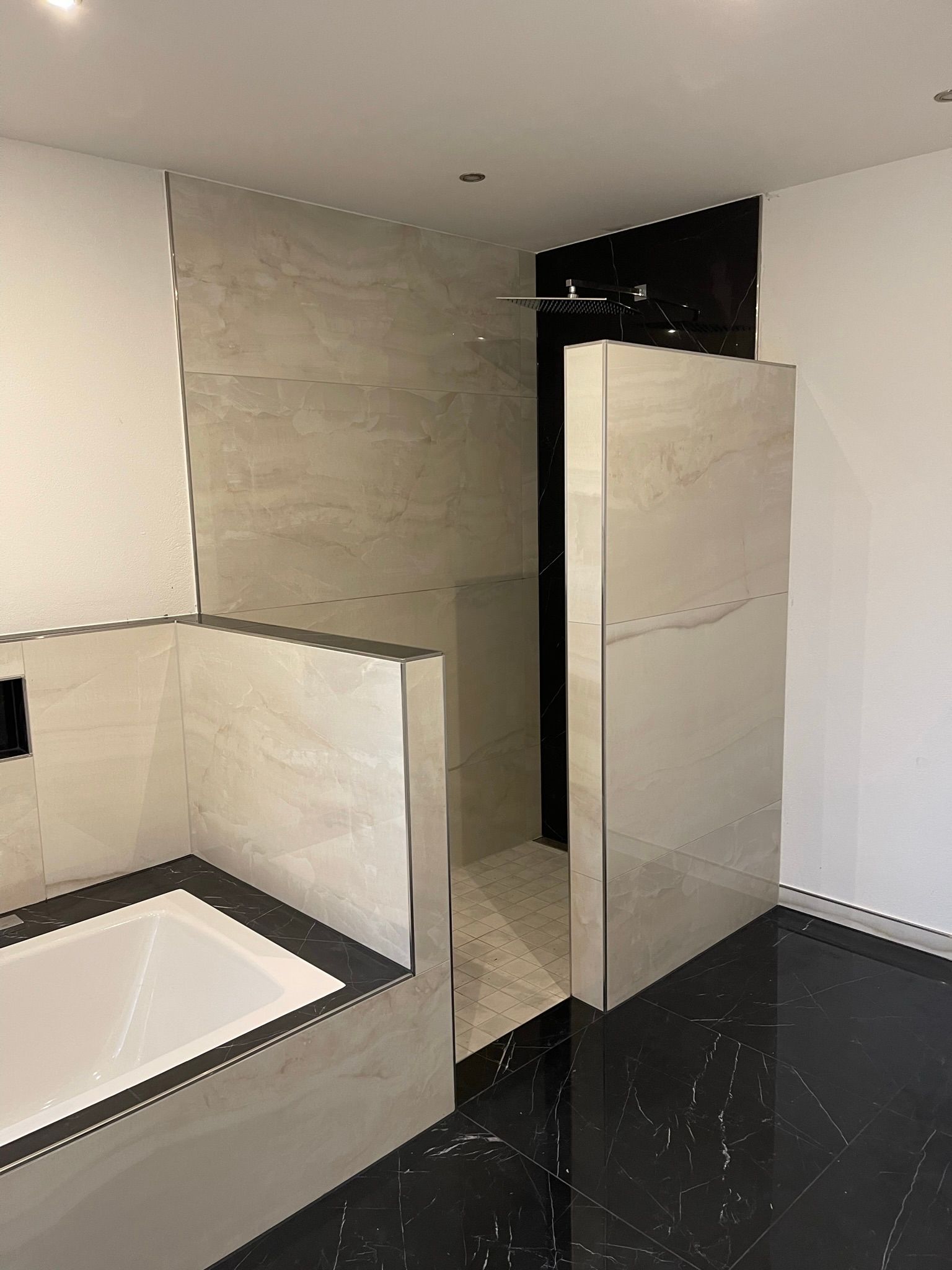 Badezimmer mit beige gefliesten Wänden, schwarz-weiß gefliestem Boden und weißer Badewanne.