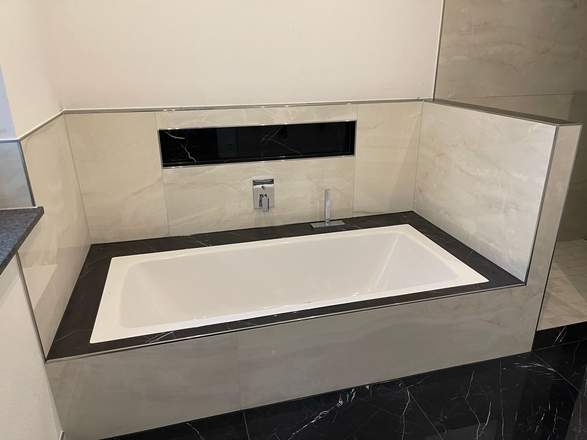 Ein modernes Badezimmer mit einer eingebauten weißen Badewanne, umrahmt von schwarzen und hellgrauen Fliesen.