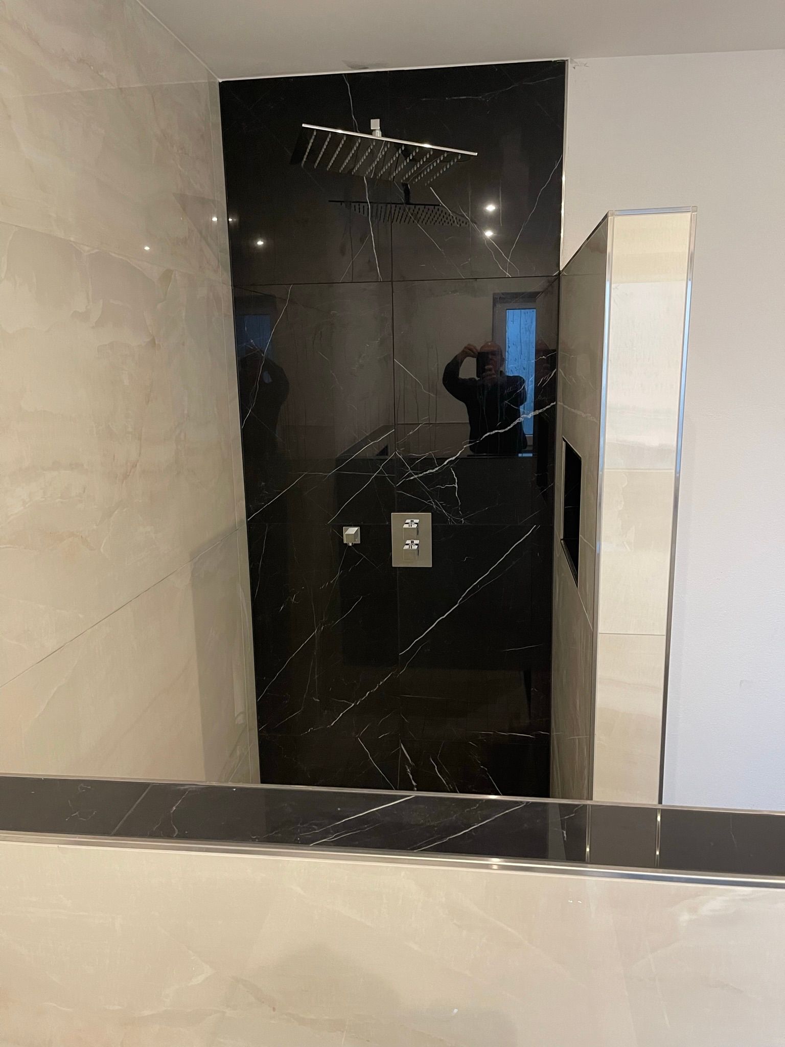 Ein modernes Badezimmer mit schwarzer Duschkabine, verspiegelten Akzenten und hellen Wänden.