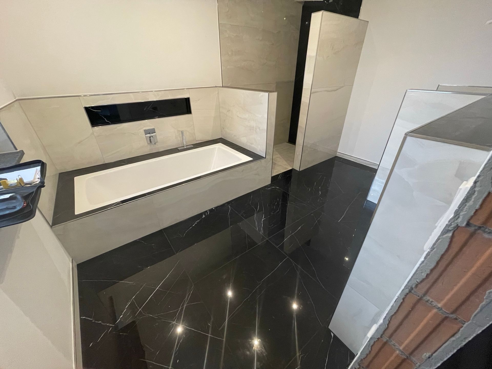 Im Bau befindliches schwarz-weiß gefliestes Badezimmer mit Badewanne und offener Tür.