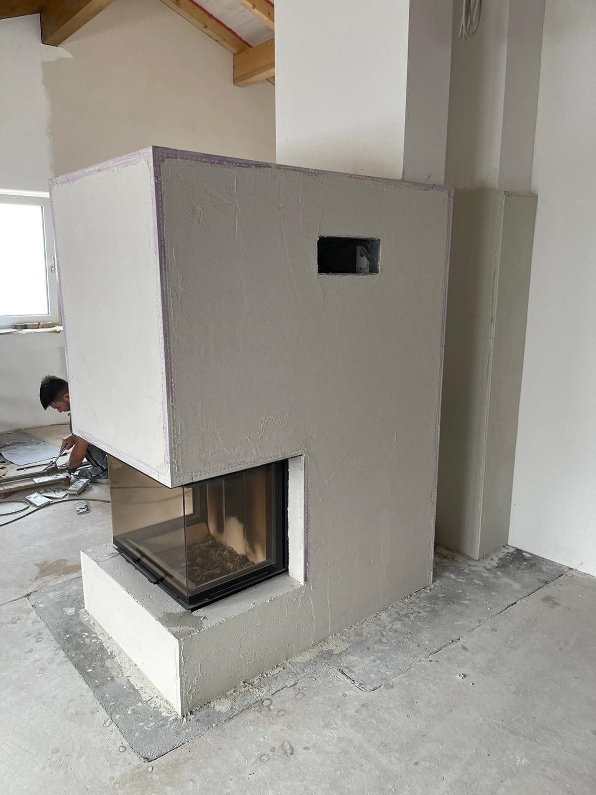 Kamin im Bau, hellgrau, mit Glasfront, kleine quadratische Öffnung, Arbeiter im Hintergrund.