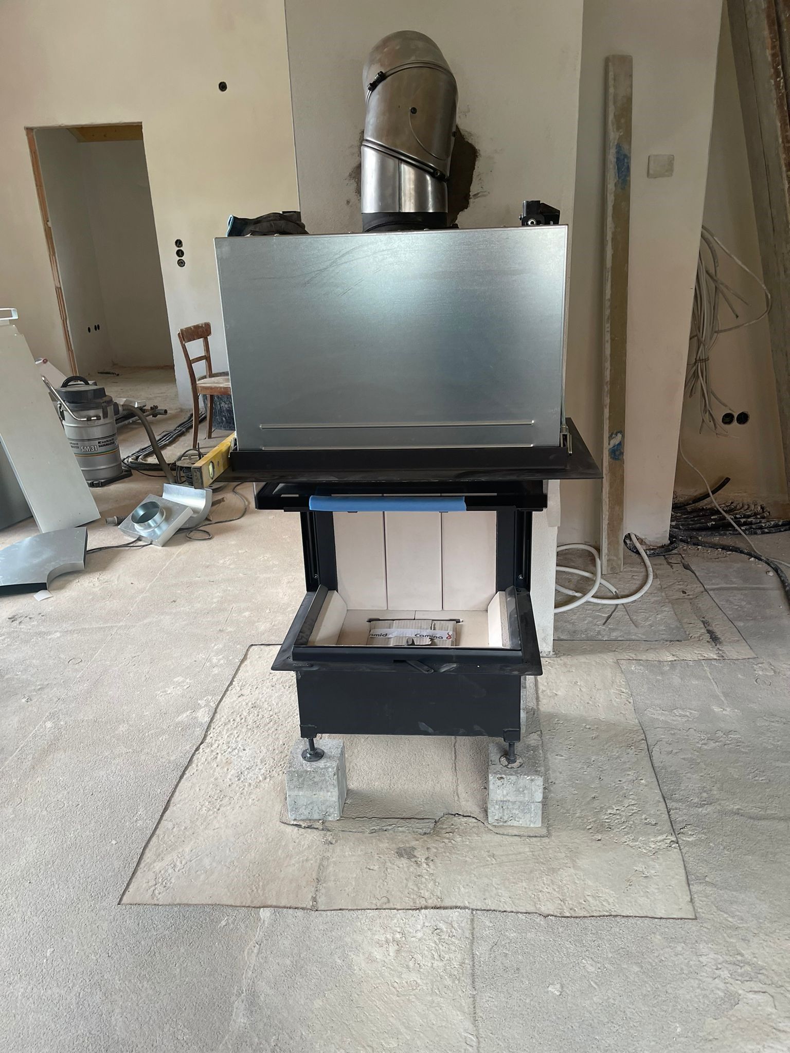 Ein Kamin mit einem Metallkamin, der während der Bauarbeiten im Innenbereich auf Betonblöcken installiert wurde.