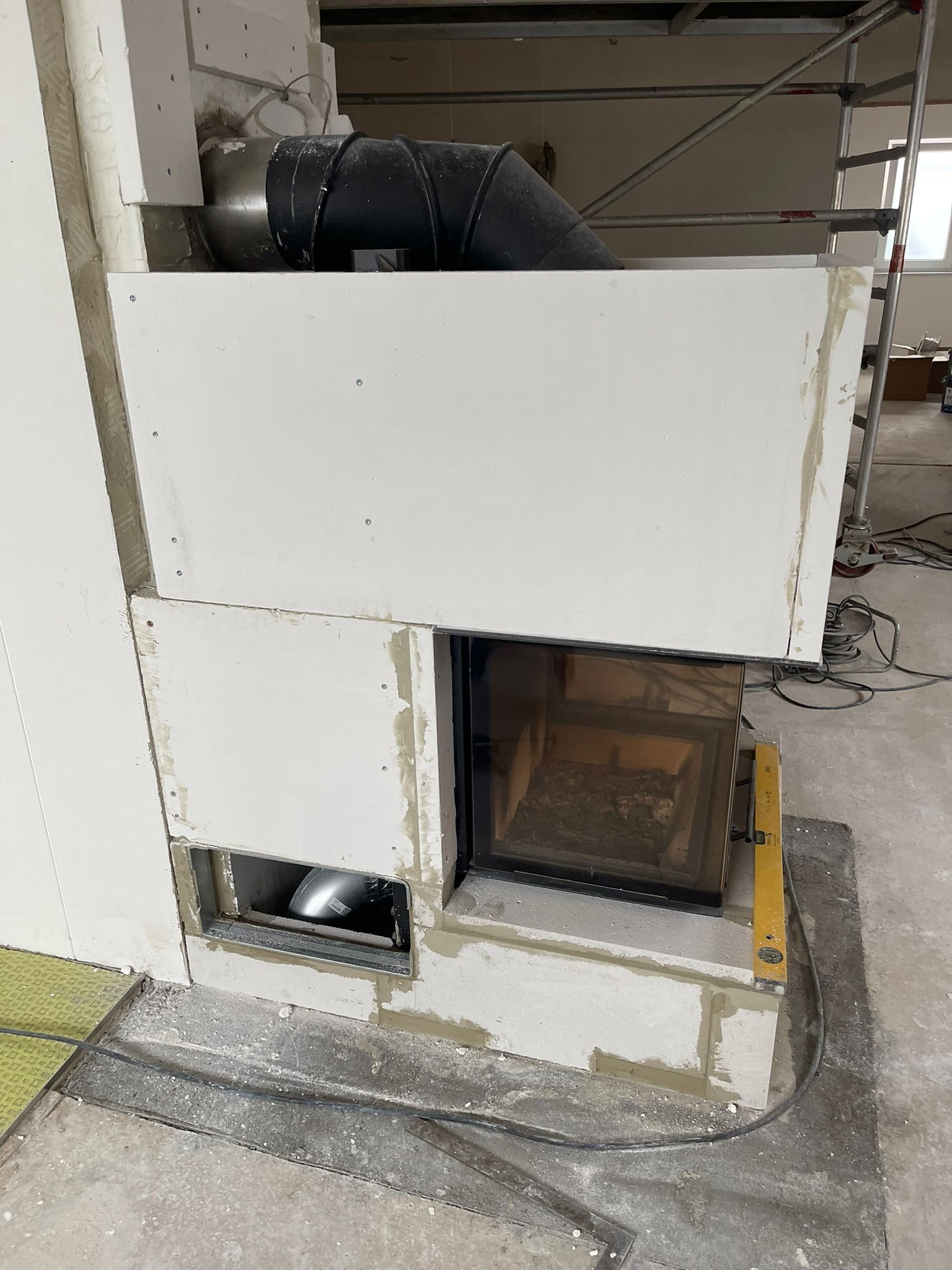 Teilweise aufgebauter Kamin mit weißen Paneelen, einer schwarzen Entlüftung und einer Glastür.