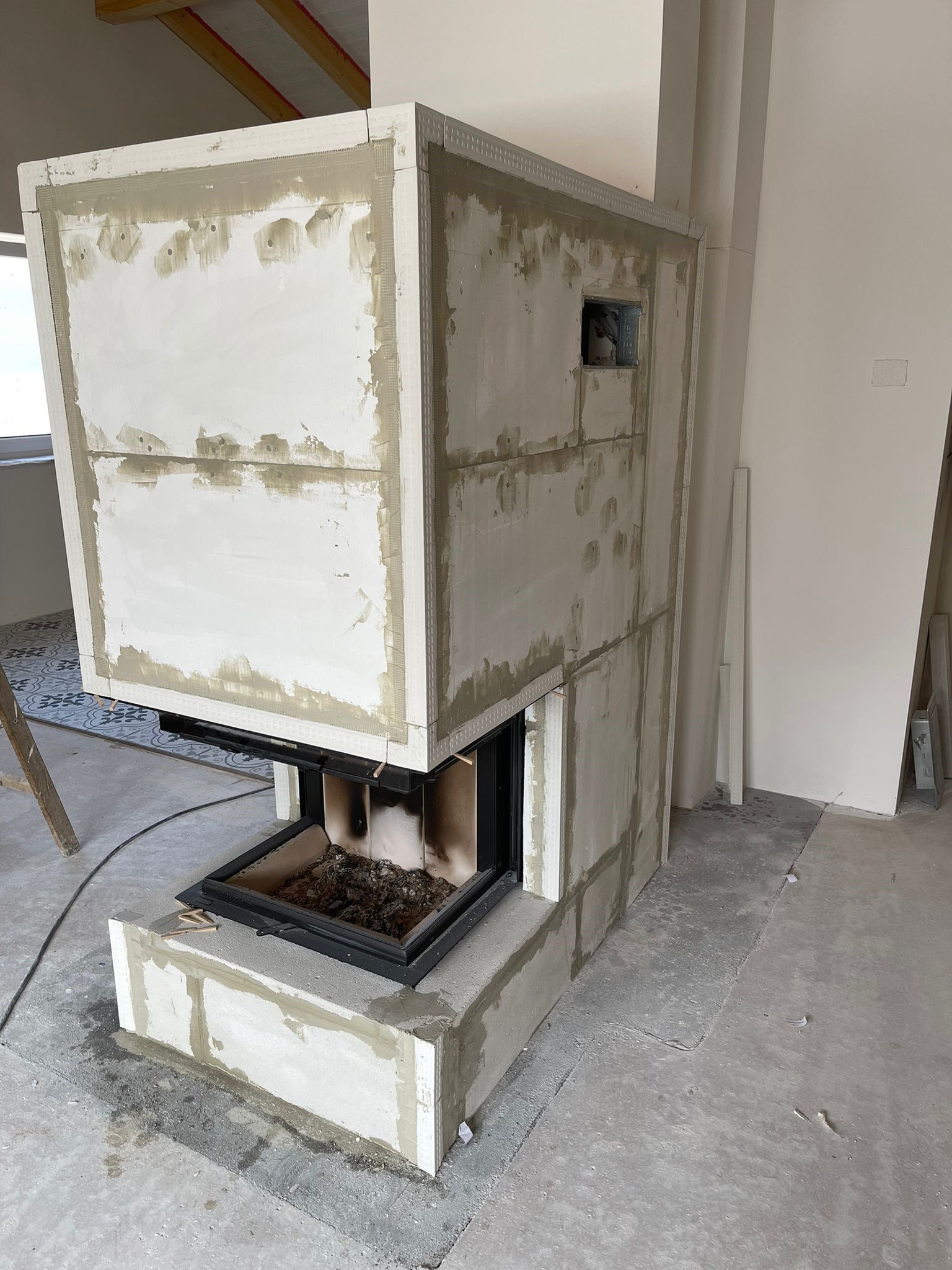 Ein teilweise aufgebauter Kamin. Weiße Blöcke und grauer Mörtel umgeben den schwarzen Feuerraum.