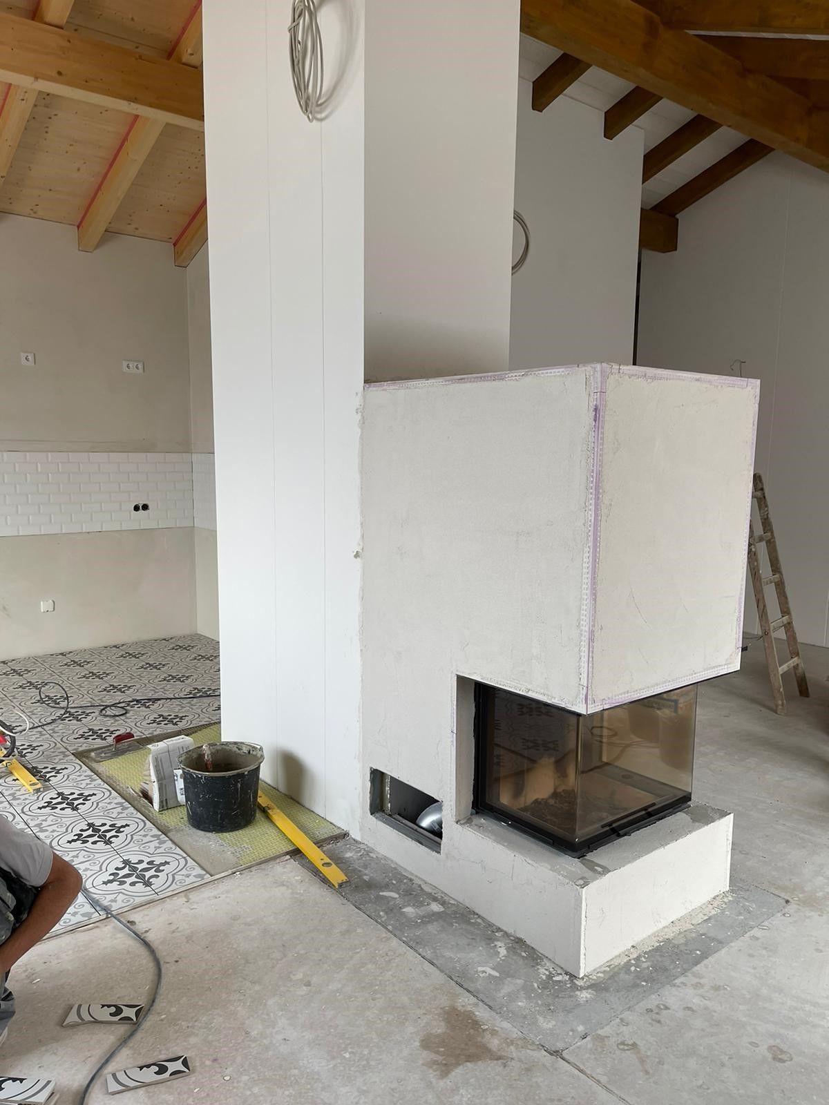 Ein weißer Kamin im Bau. Eine Person arbeitet am Boden. Im Hintergrund steht eine Leiter.
