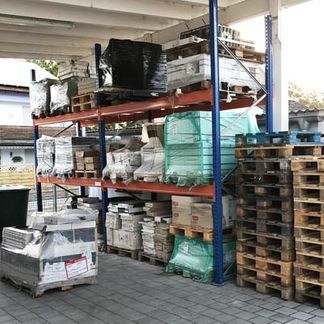 Draußen unter einem Dach stehen Regale voller verpackter Kisten, Paletten und Ausrüstung.