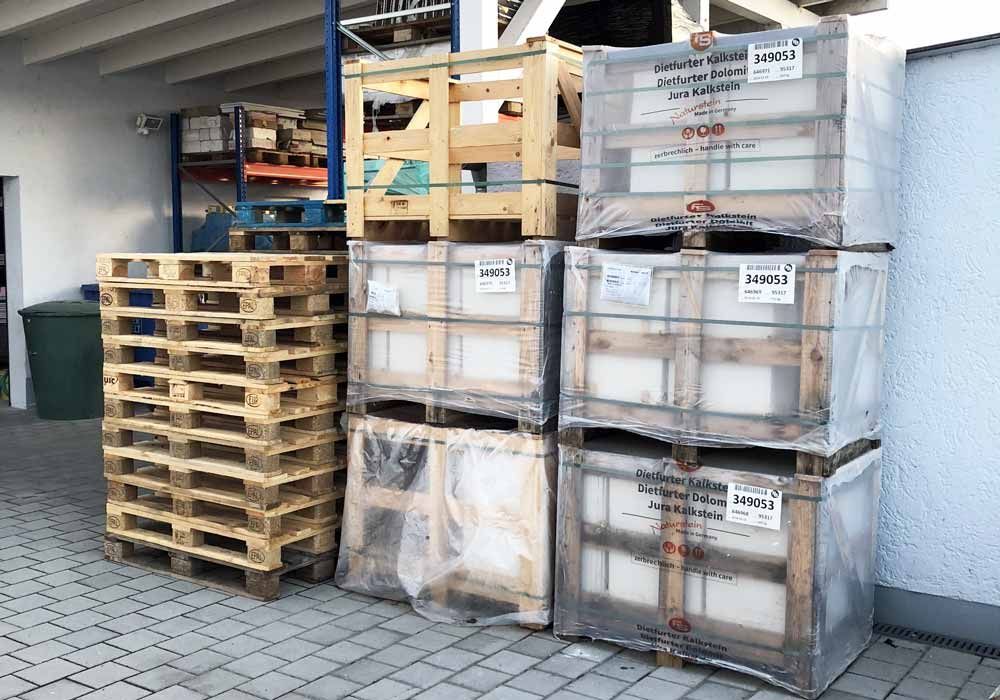 Holzkisten und Paletten sind im Freien an einem Gebäude gestapelt.