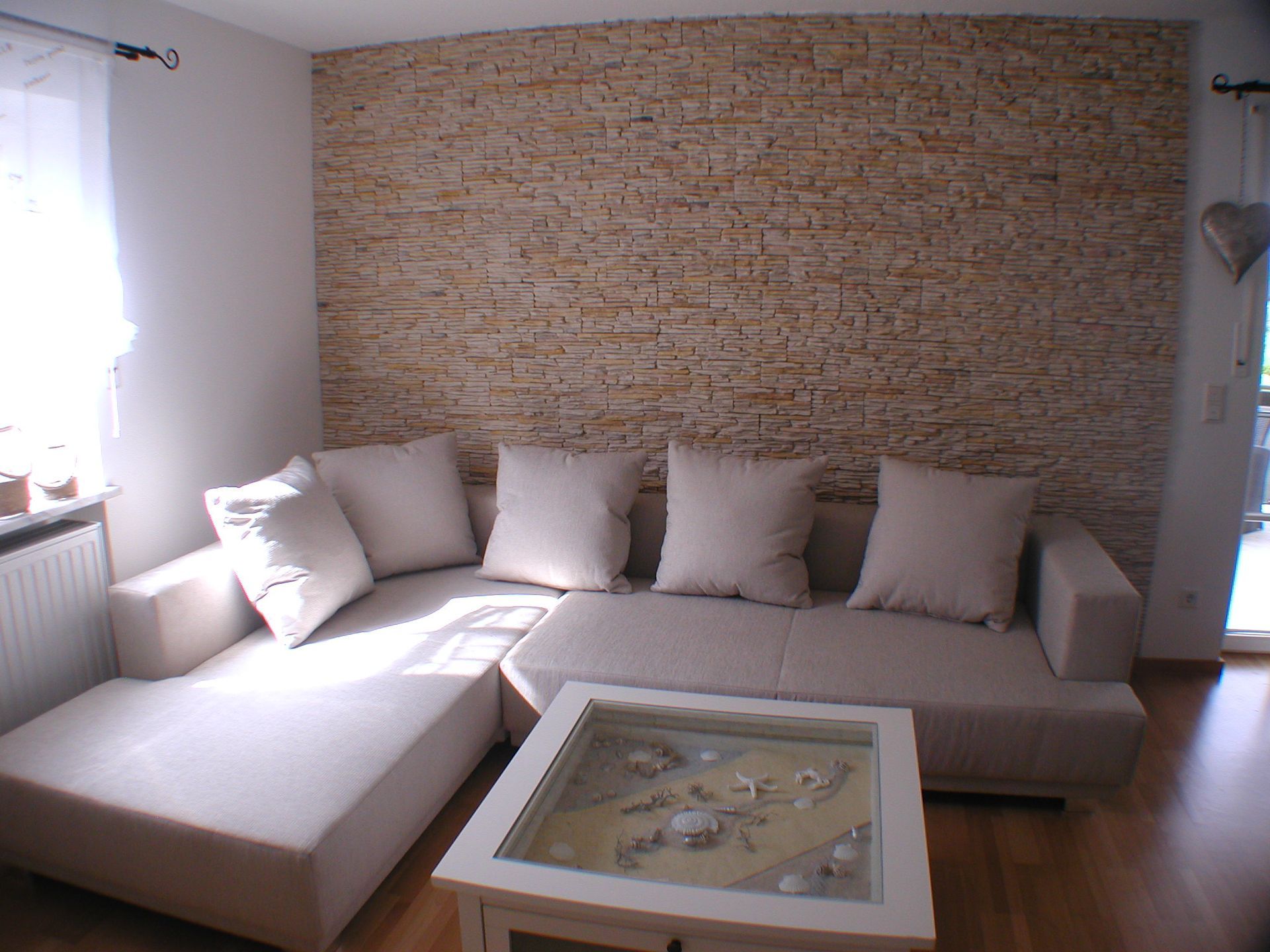 Beiges Sofagarnitur in einem Wohnzimmer mit einer Akzentwand aus Stein und einem Couchtisch mit Glasplatte.