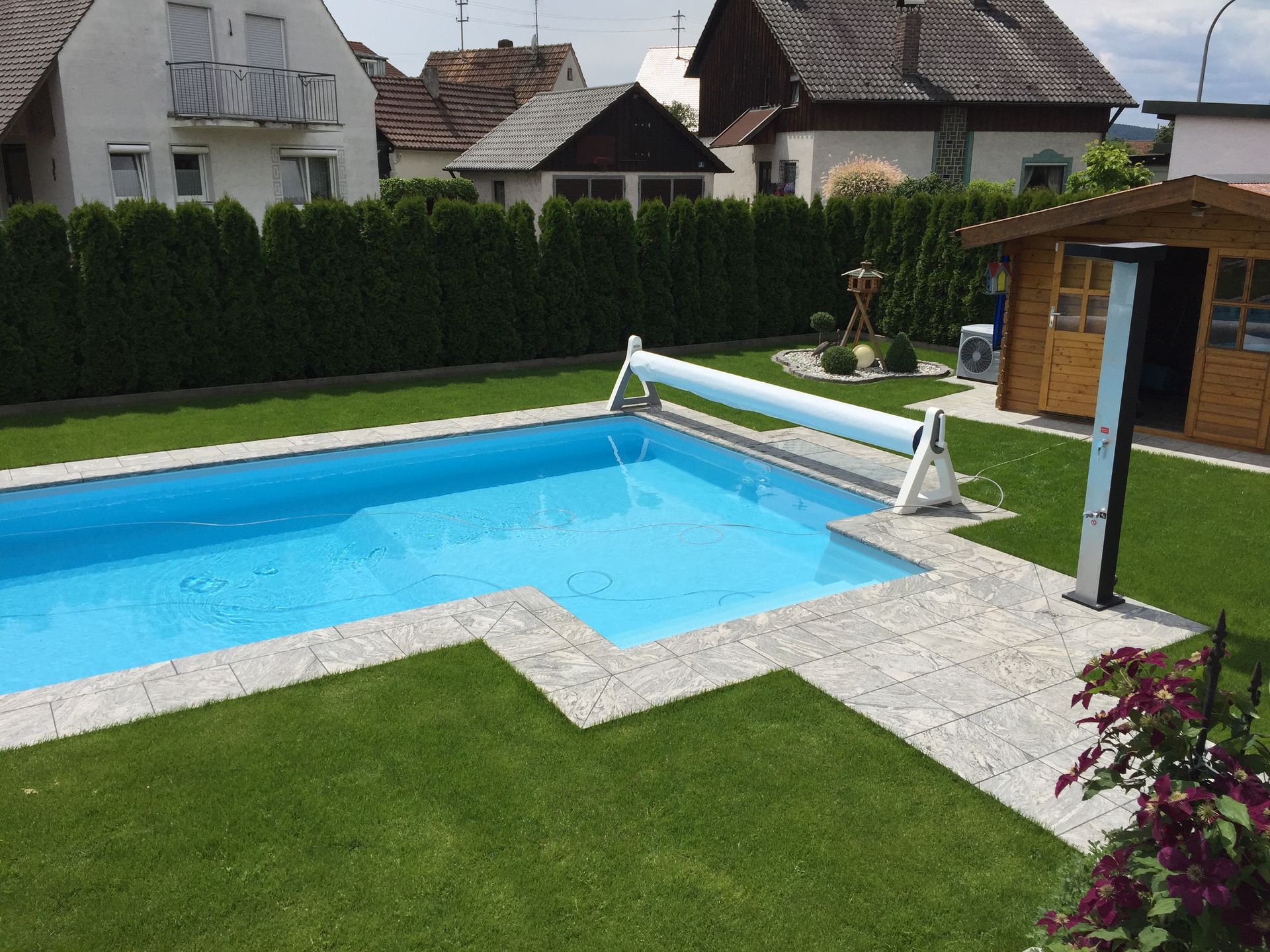 Ein rechteckiger Swimmingpool in einem Hinterhof mit einem kleinen Holzschuppen und grünem Gras.