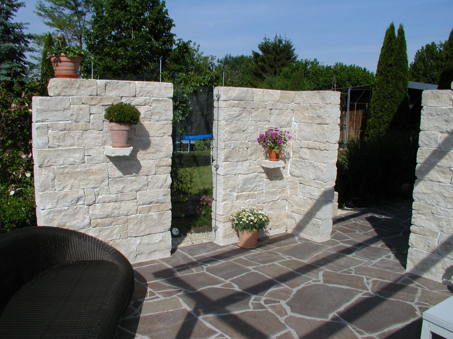 Steingartenmauern mit Topfpflanzen schaffen einen privaten Außenbereich; sonniger Tag.