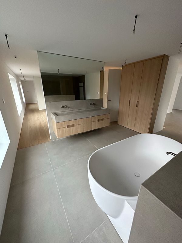 Modernes Badezimmer mit schwebendem Waschtisch, Badewanne und Holzschränken; hellgraue Fliesen.