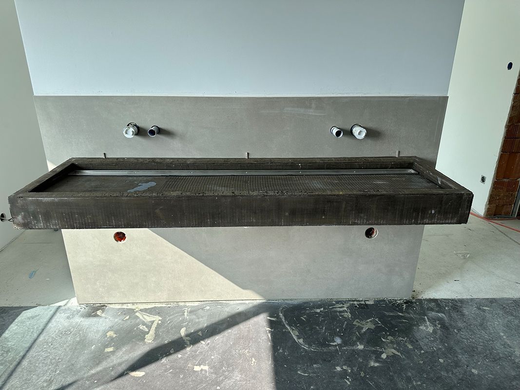 Graues Steinwaschbecken und Spritzschutz in einer Baustellenumgebung, zwei Wasserhähne.