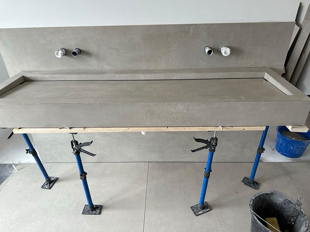 Betonarbeitsplatte wird von verstellbaren Hebern getragen, an der Wand sind Rohre sichtbar. Bauumgebung.