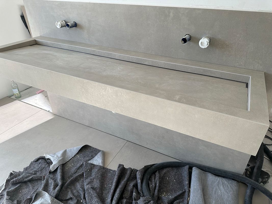 Eine Badezimmertheke aus grauem Beton mit Rohrleitungen und Werkzeugen auf dem Boden.