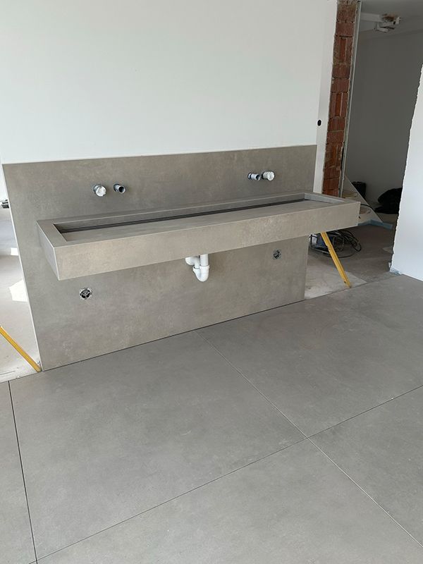 Graues Waschbecken aus Beton an einer weißen Wand, in der Nähe eines unfertigen Fußbodens.