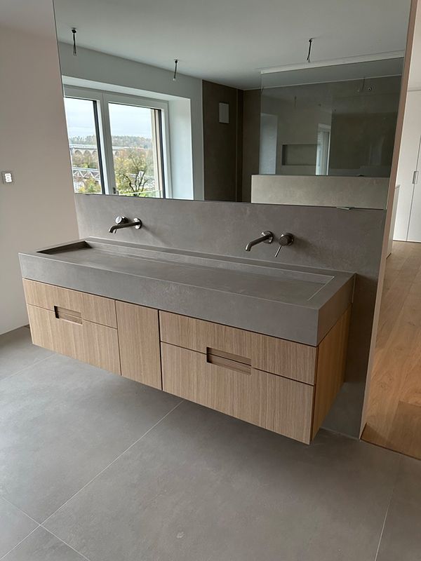 Schwebender Badezimmerwaschtisch mit Holzschränken, Betonarbeitsplatte und wandmontierten Wasserhähnen.
