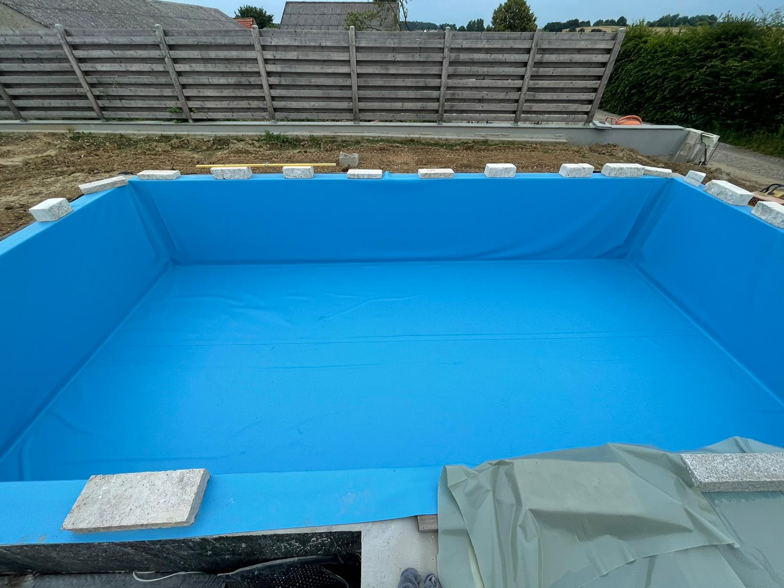 Ein im Bau befindlicher rechteckiger Pool mit blauer Umrandung und Betonblöcken und einem Holzzaun im Hintergrund.