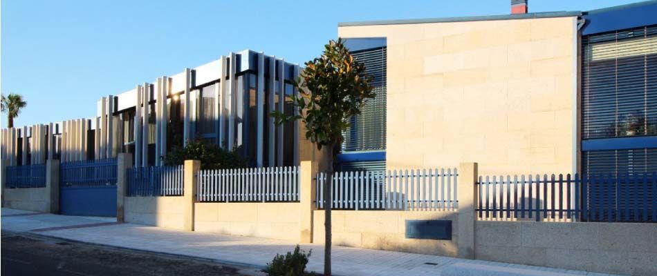 Un edificio con una valla azul y un árbol delante.