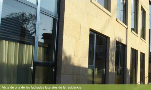 Un edificio con muchas ventanas y una leyenda que dice vista de una de las fachadas laterales de la residencia.