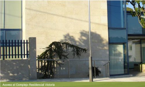 Un edificio con una valla y un árbol delante.