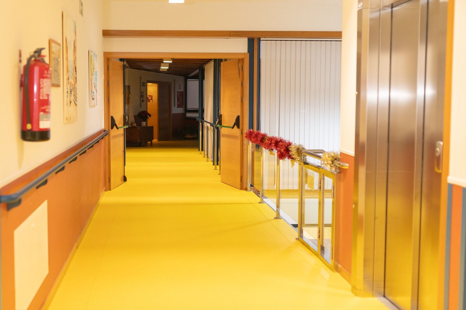 Un pasillo largo con piso amarillo y un extintor en la pared.