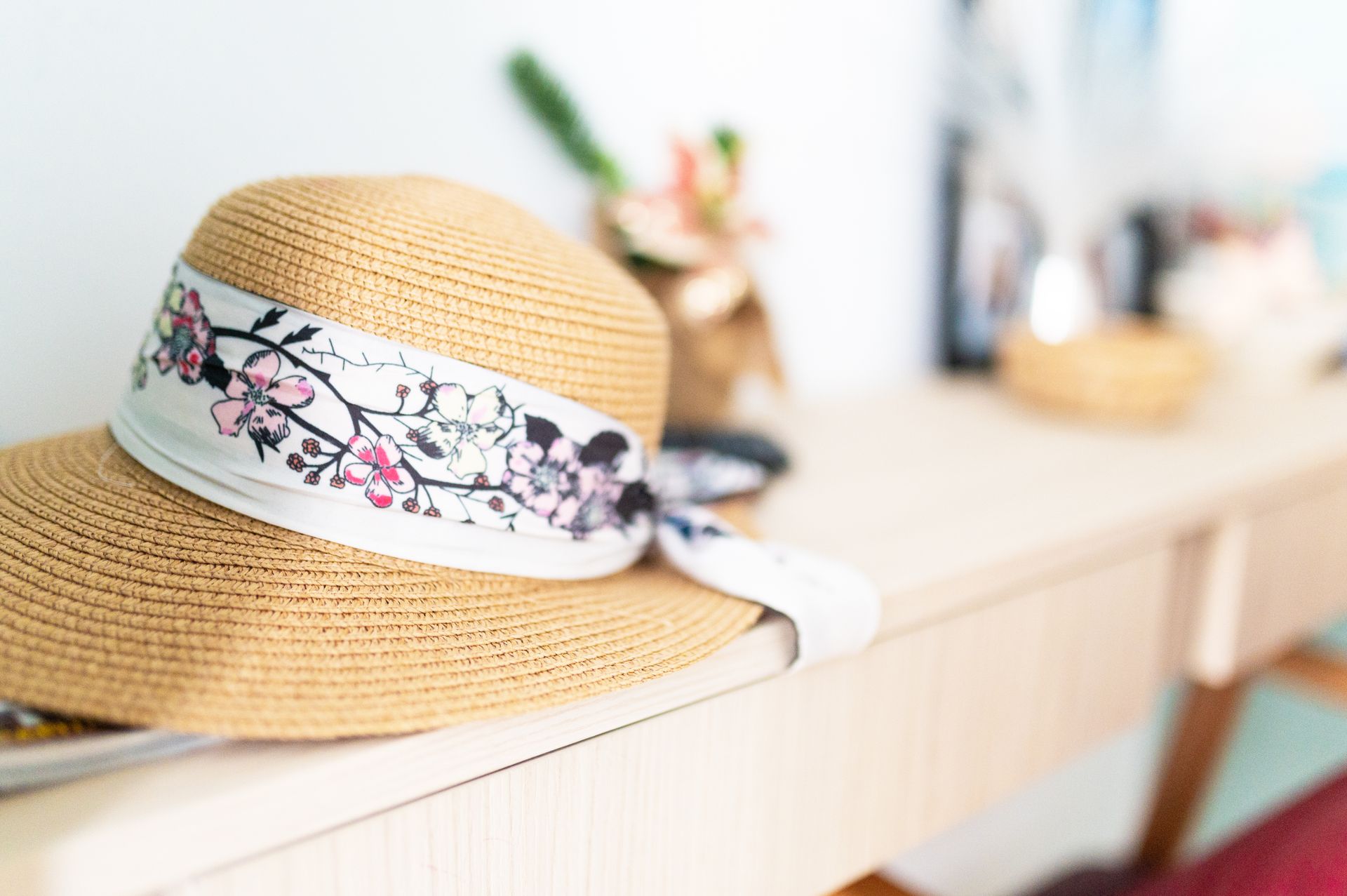 Un sombrero de paja con una cinta floral está sobre una mesa.