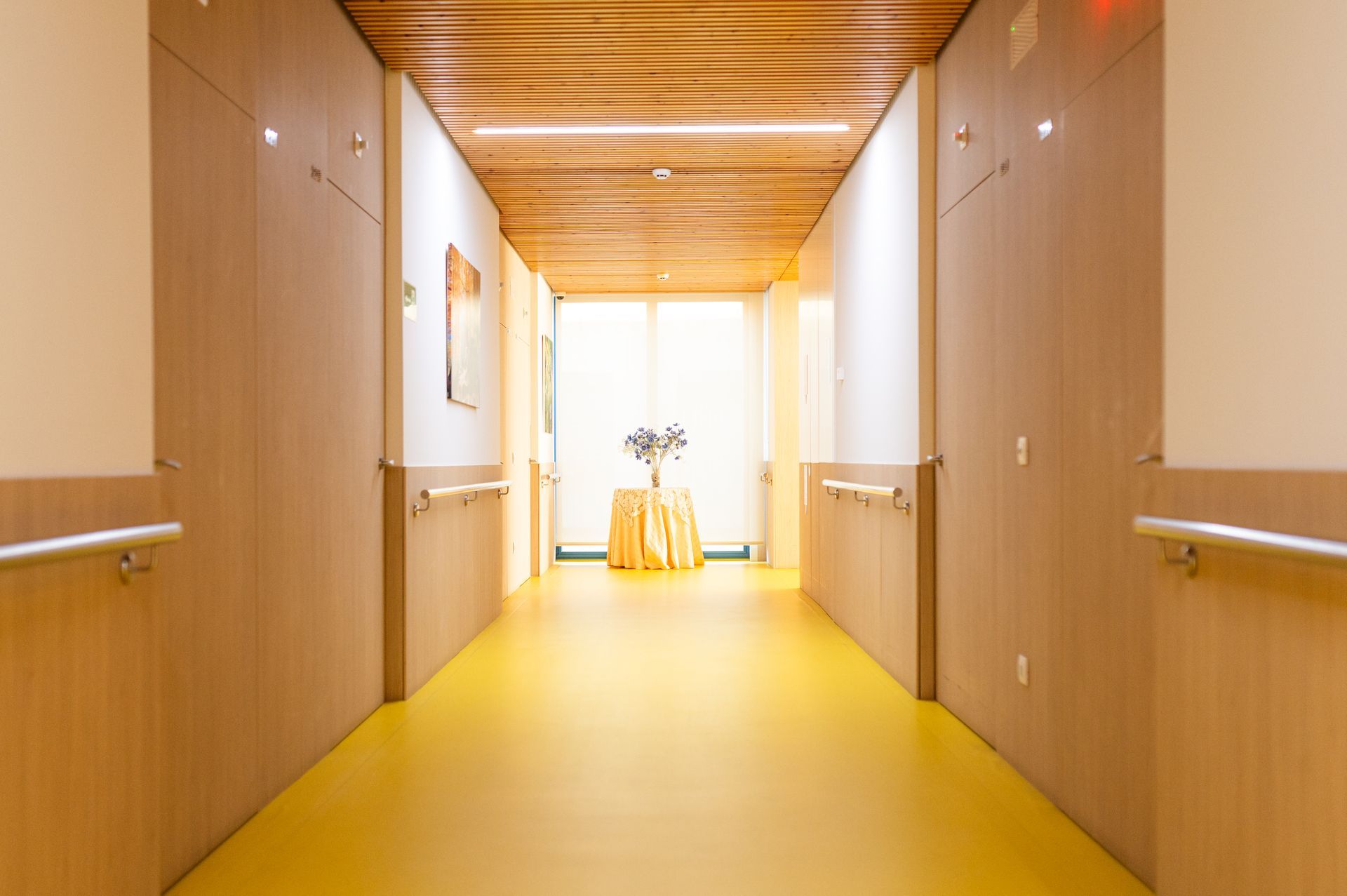 Un largo pasillo con suelo amarillo y paredes de madera en un hospital.