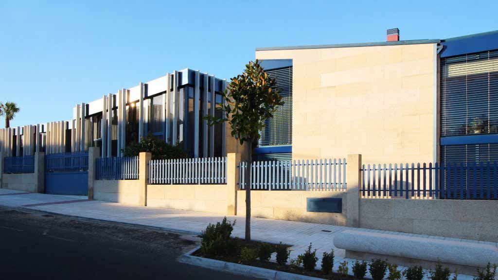 Un edificio con una valla azul y un árbol delante.