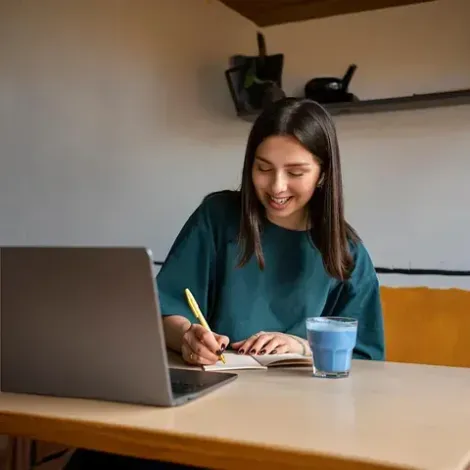 Una mujer está sentada en una mesa con una computadora portátil y un vaso de agua.