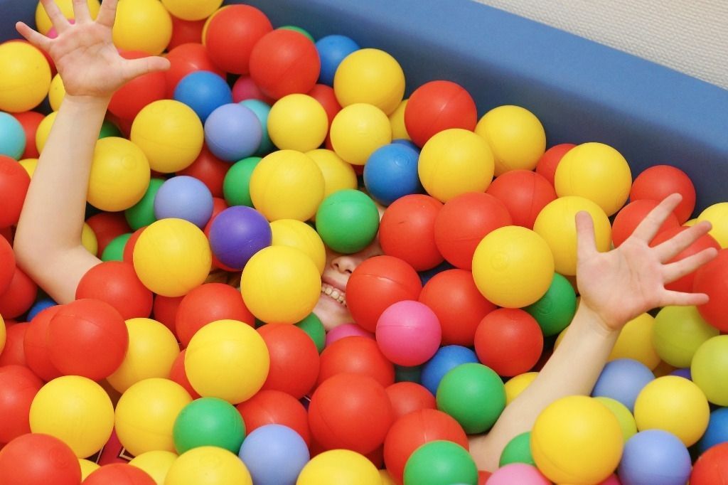 Lapsi värikkäässä pallomeressä vain kädet ja hymyilevät kasvot näkyvillä; Activus Oy:n terapiaympäristö