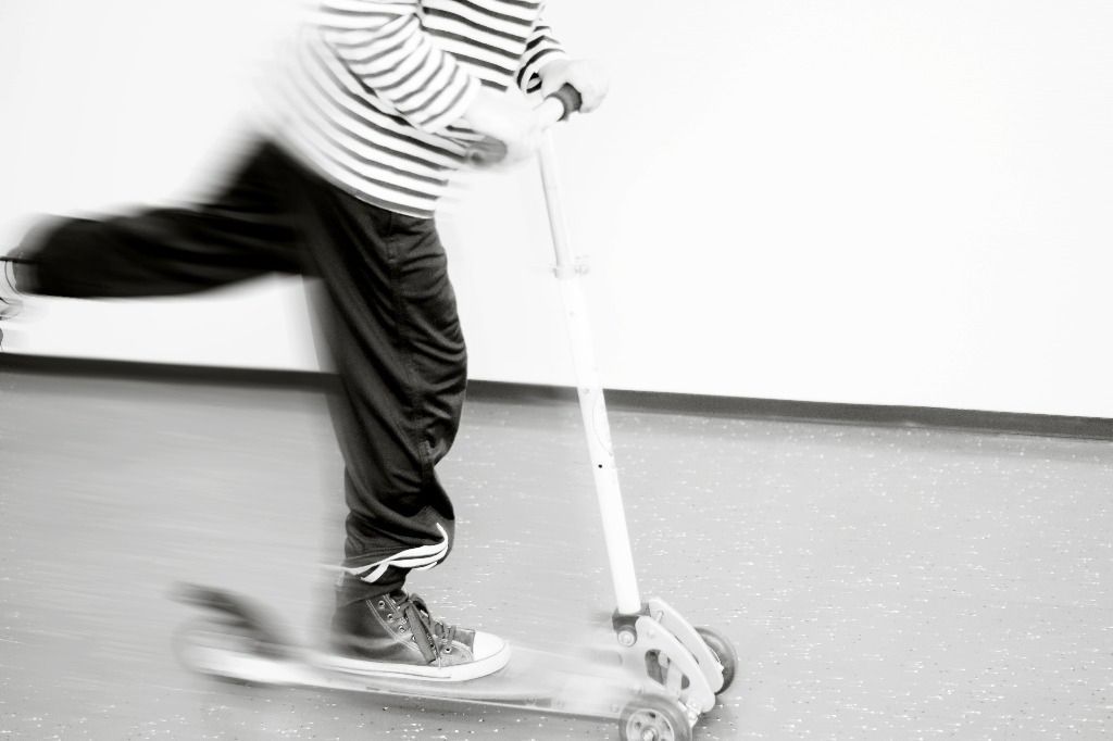 Lapsi potkii potkulaudalla, sumea liike, mustavalkoinen; Activus Oy:n terapiaympäristö