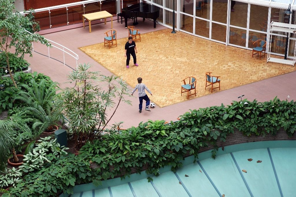 Kaksi ihmistä pelaa jalkapalloa sisäpihalla, jossa on kasveja, tuoleja ja piano; Activus Oy:n terapiaympäristö