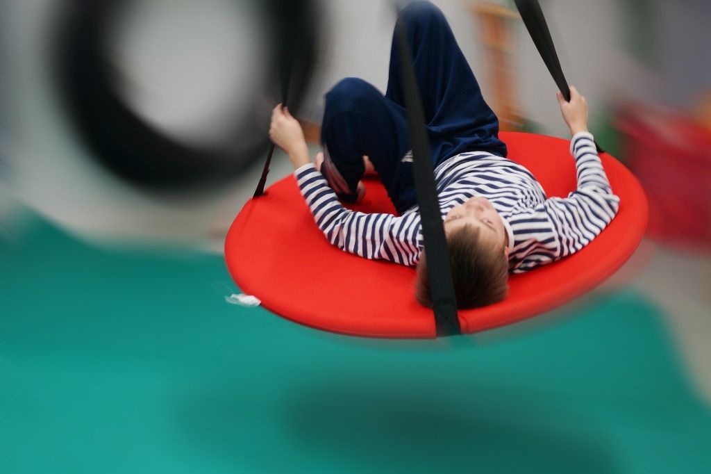 Lapsi keinuu pyöreällä keinulla maaten; Activus Oy:n terapiaympäristö