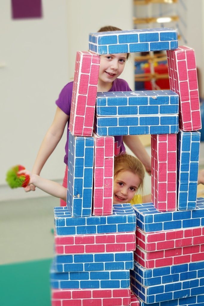 Lapsi kurkkaa palikoista rakennetun rakennelman takaa iloisena; Activus Oy:n terapiaympäristö