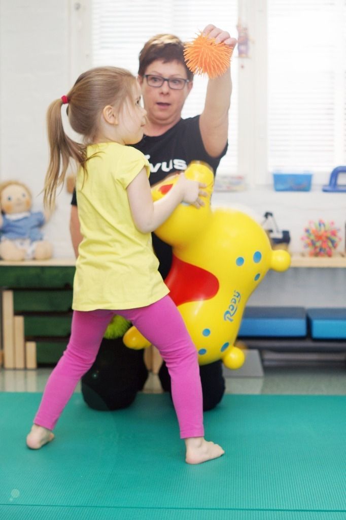 Lapsi kurkottaa terapeutin kädessä olevaan leluun; Activus Oy:n terapiaympäristö