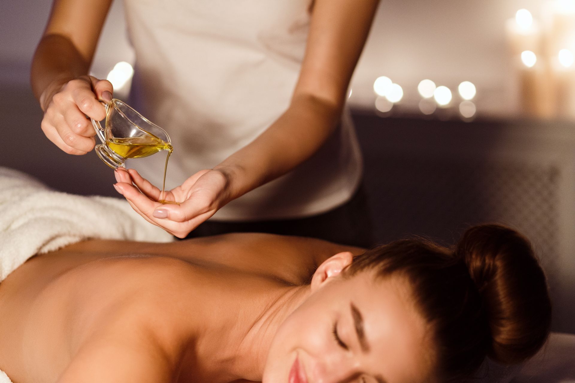 Eine Spa-Therapeutin giesst während einer Massage Öl auf den Rücken einer Frau.