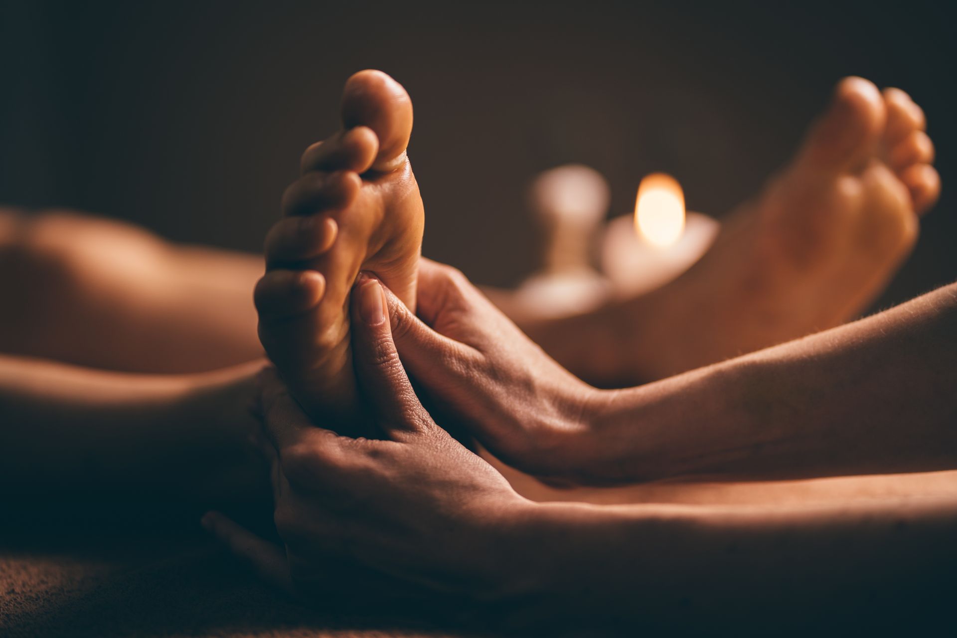 In einer warmen, sanft beleuchteten Spa-Atmosphäre mit verschwommenem Kerzenlicht im Hintergrund massieren Hände Füsse.