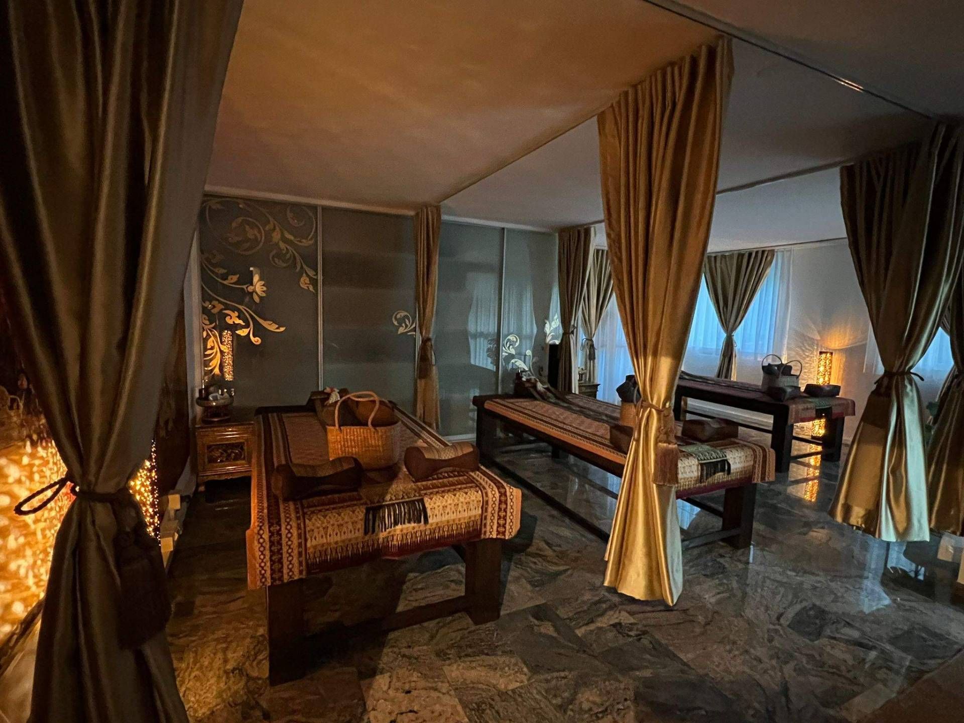 Luxuriöse Lounge im Freien mit Korbsesseln, drapierten Vorhängen und einem atemberaubenden Blick auf den Sonnenuntergang über dem Wasser bei Kerzenschein.