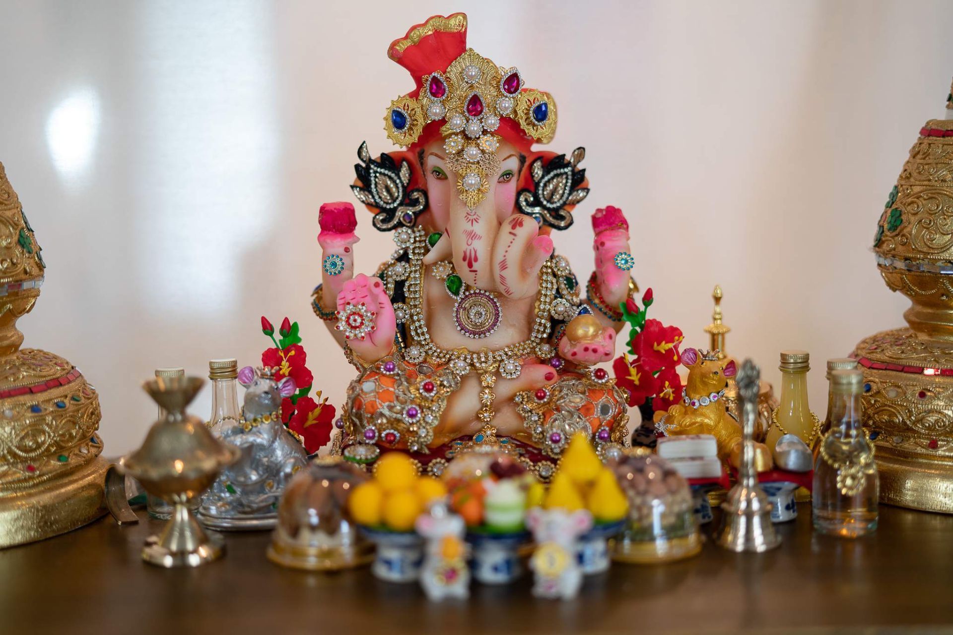 Ganesha-Statue auf einem Hausaltar mit Opfergaben, kleinen Figuren und Messingdekoration