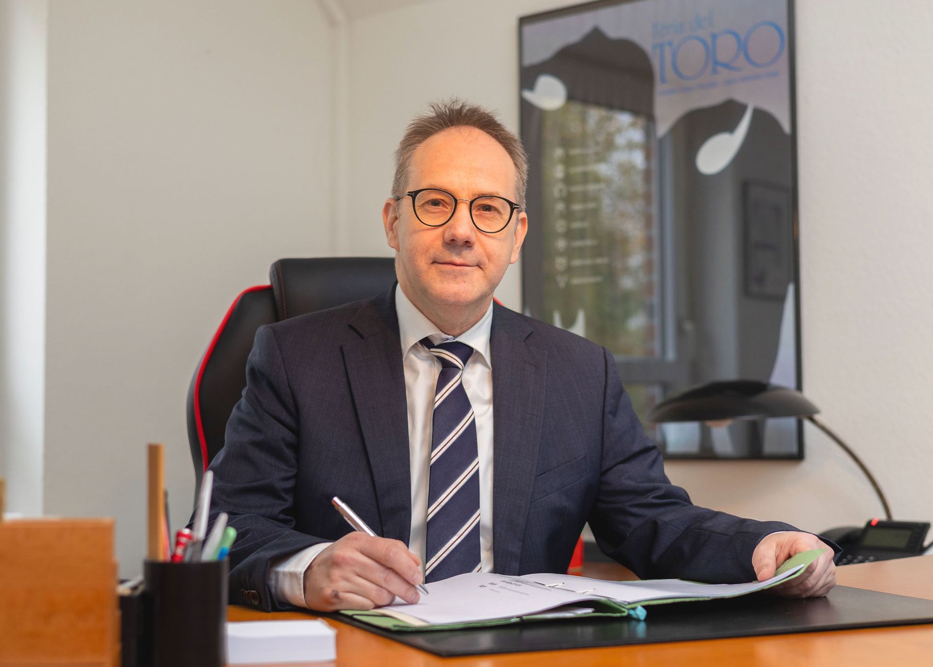 Ein Mann in Anzug und Krawatte sitzt an einem Schreibtisch