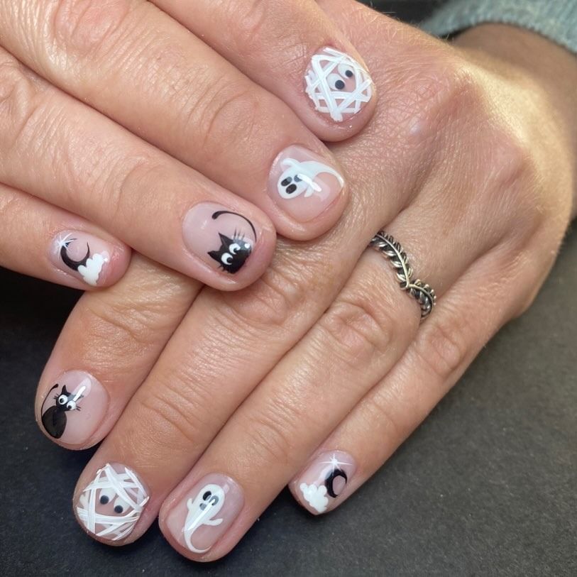 Las uñas de una mujer están decoradas con gatos y fantasmas en blanco y negro.