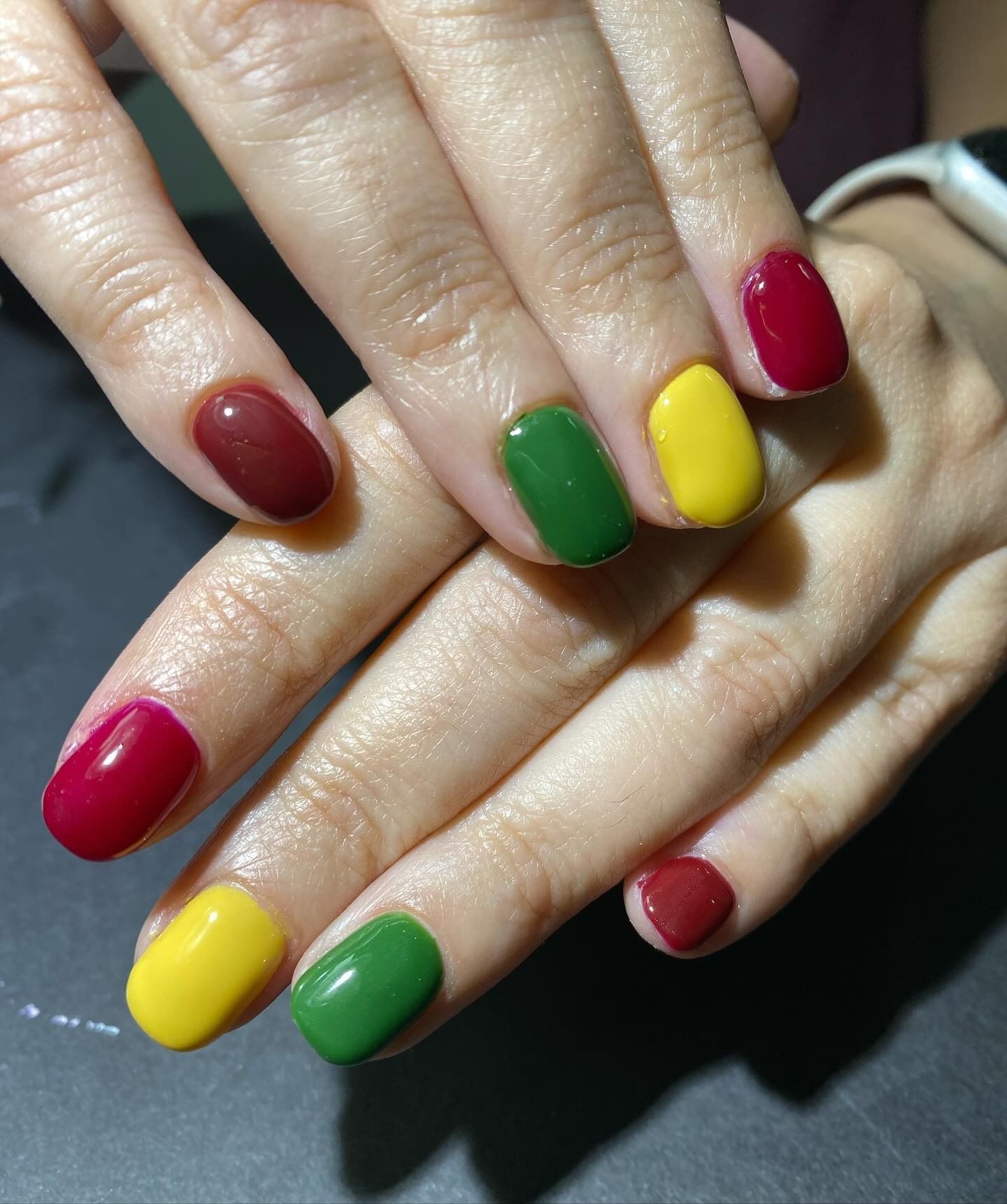 Las uñas de una mujer están pintadas de rojo, verde y amarillo.