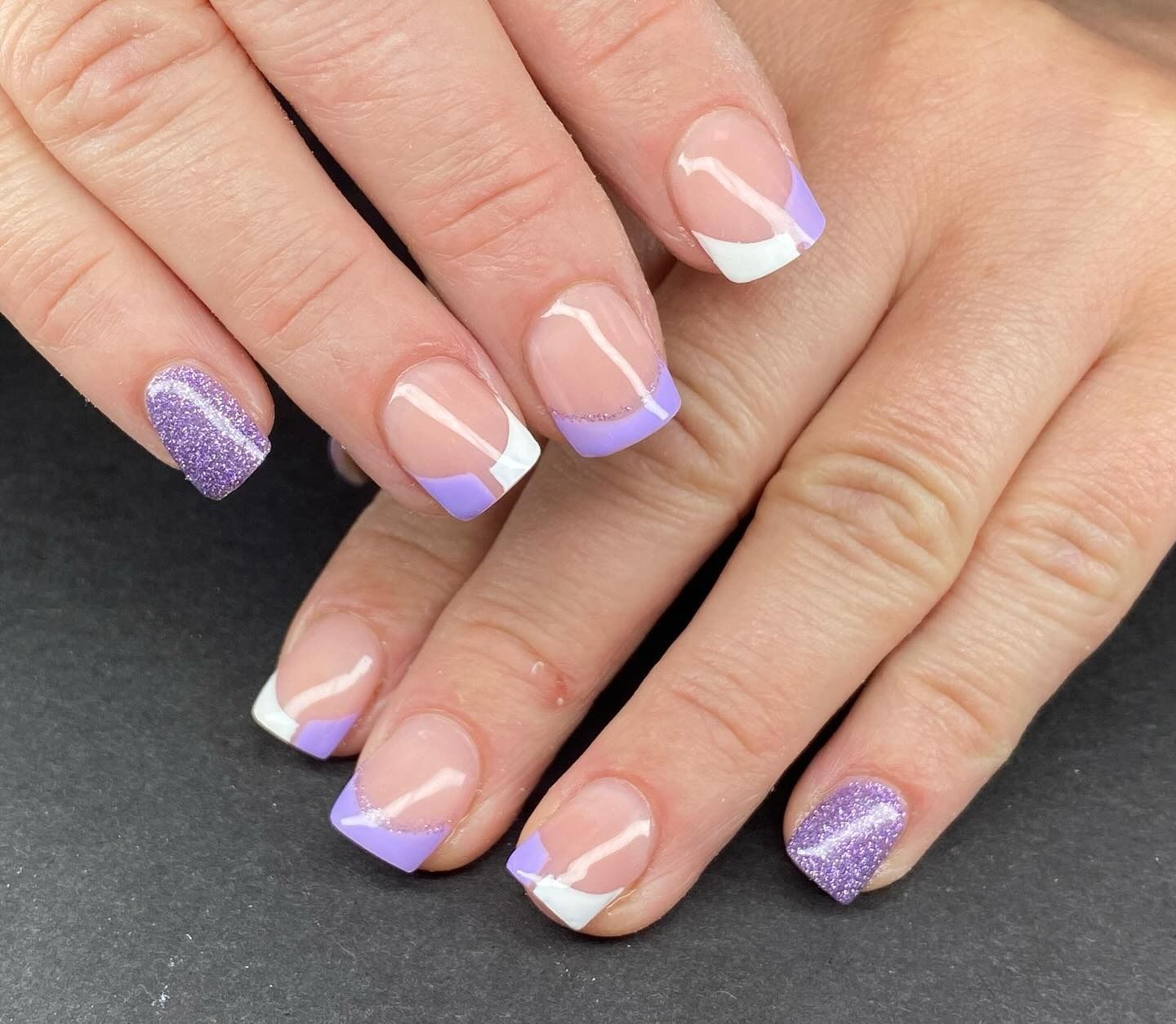 Un primer plano de las uñas de una mujer con manicura francesa morada y blanca.