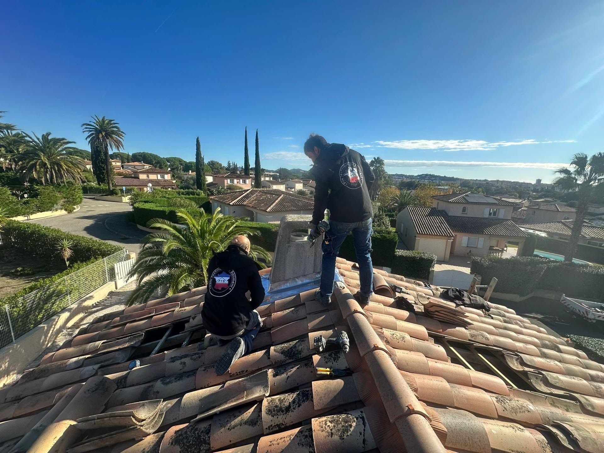 Deux personnes sur un toit surplombant un quartier côtier ensoleillé et un ciel bleu.